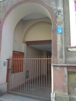 Zdjęcie przedstawia dużą  bramę wejściową do budynku, w krórym  znajduje się lokal mieszkalny na sprzedaż.